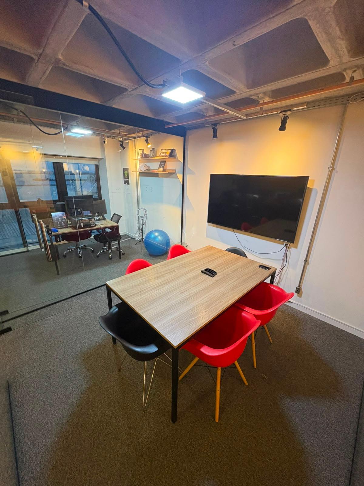 Sala de reunião privativa com TV 65", mesa e cadeiras vermelhas no cubo de vidro